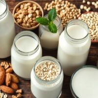 Various milk alternatives with fresh ingredients on wooden surface.